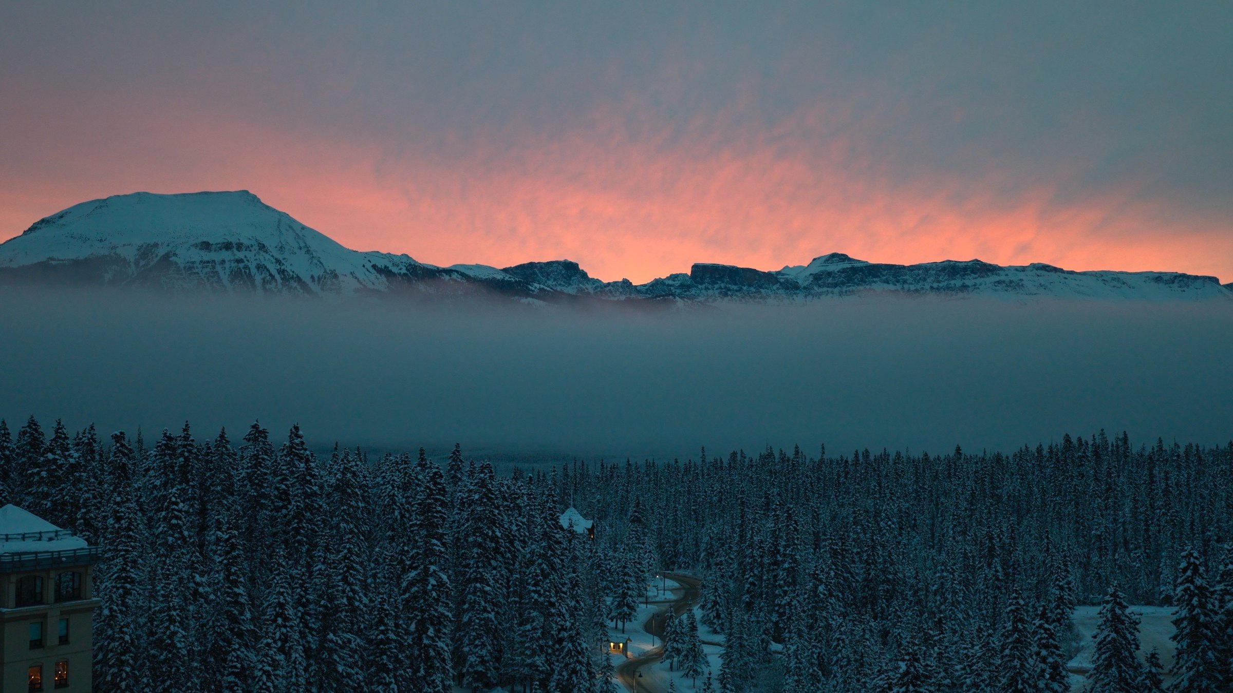 Sunset over snow-covered mountains above a valley of fog and pine forest